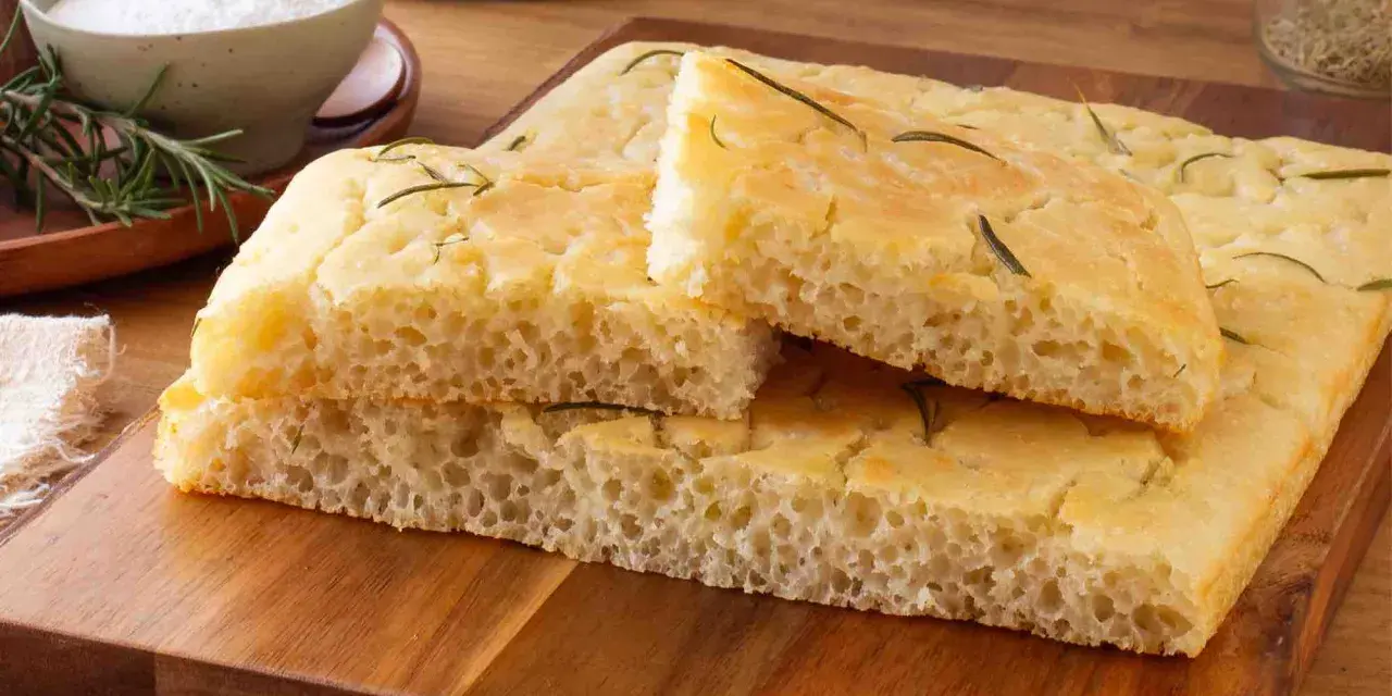 Focaccia senza glutine soffice e dorata, guarnita con rosmarino fresco, pronta per essere gustata.