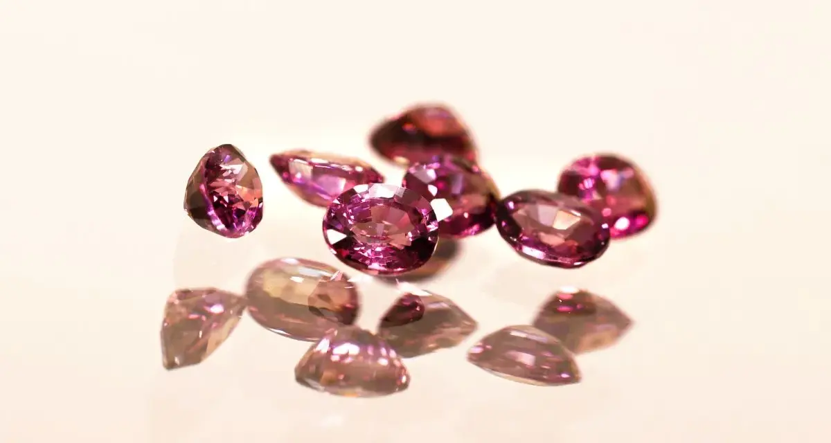 Un gruppo di pietre di granato rosa sfaccettate, che riflettono la luce su una superficie lucida.