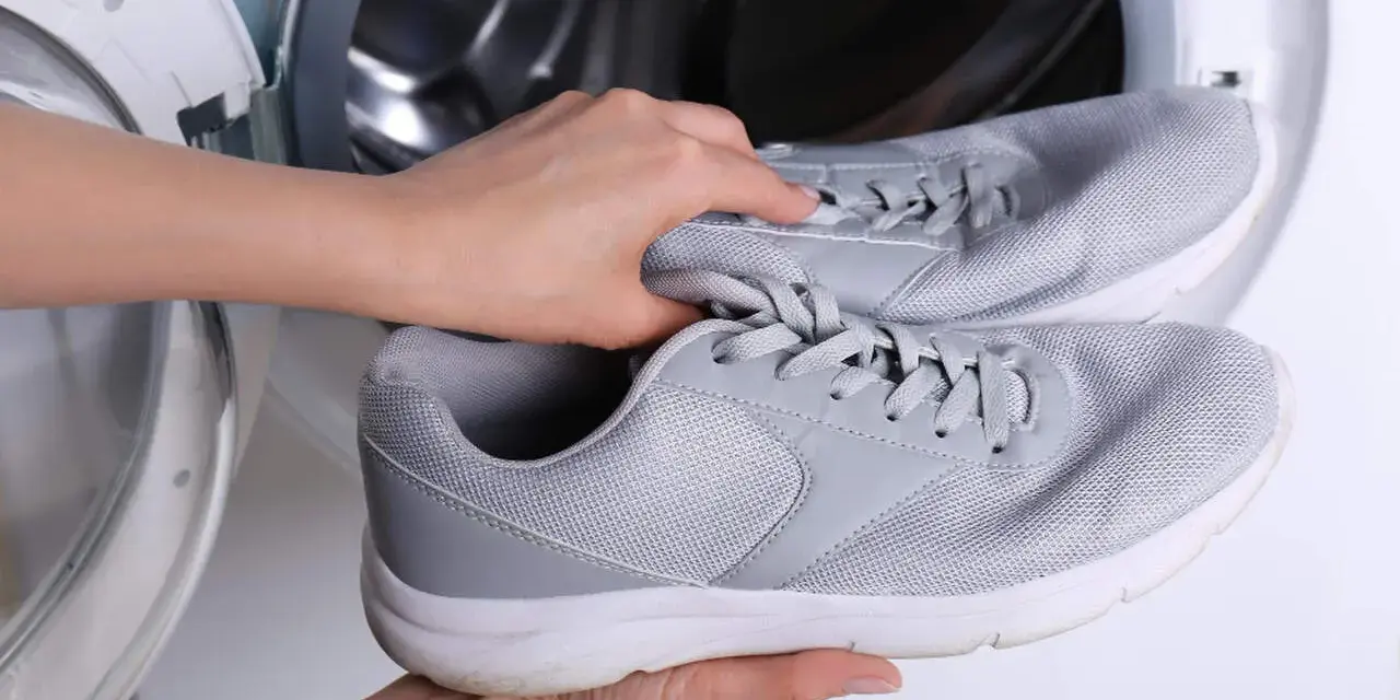 Ręce wkładają szare adidasy do pralki. Dowiedz się, jak prać adidasy w pralce, aby odświeżyć swoje ulubione buty.