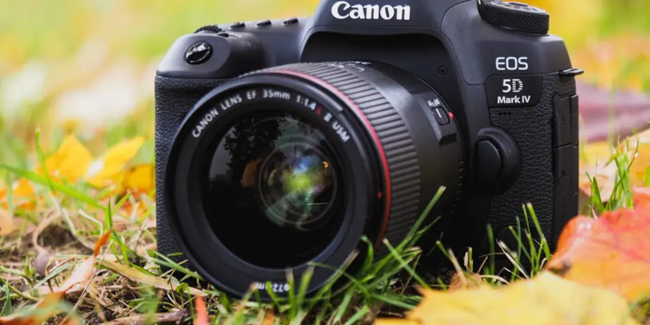 Profesjonalny aparat Canon EOS 5D Mark IV z obiektywem 35mm leży wśród jesiennych liści.