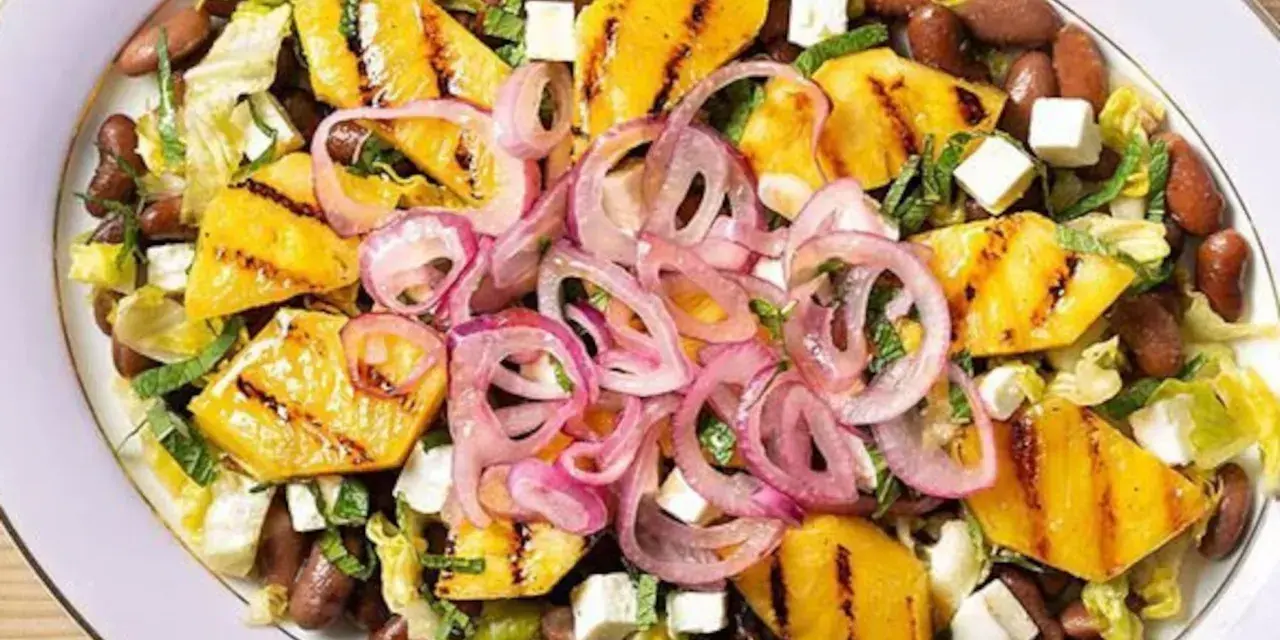 Ensalada de frijoles, piña a la parrilla, queso y cebolla morada en un plato blanco.