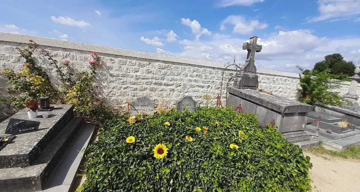 La tombe de Van Gogh, recouverte de verdure et ornée de tournesols, sous un ciel bleu.