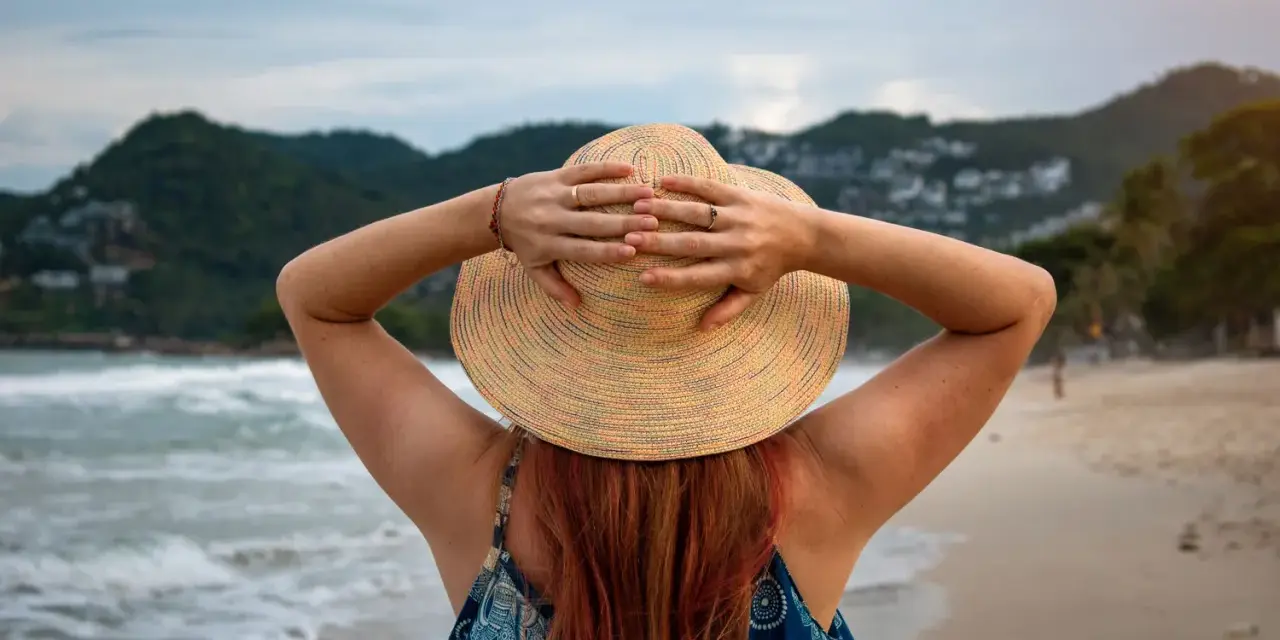 Frauenhände halten Hut am Strand. Endlich Zeit für Urlaub, der gesetzliche Urlaubsanspruch ab 50 ist wohlverdient.