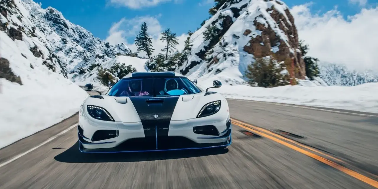 Biały Koenigsegg Agera RS z czarnym pasem na masce pędzi po ośnieżonej górskiej drodze.