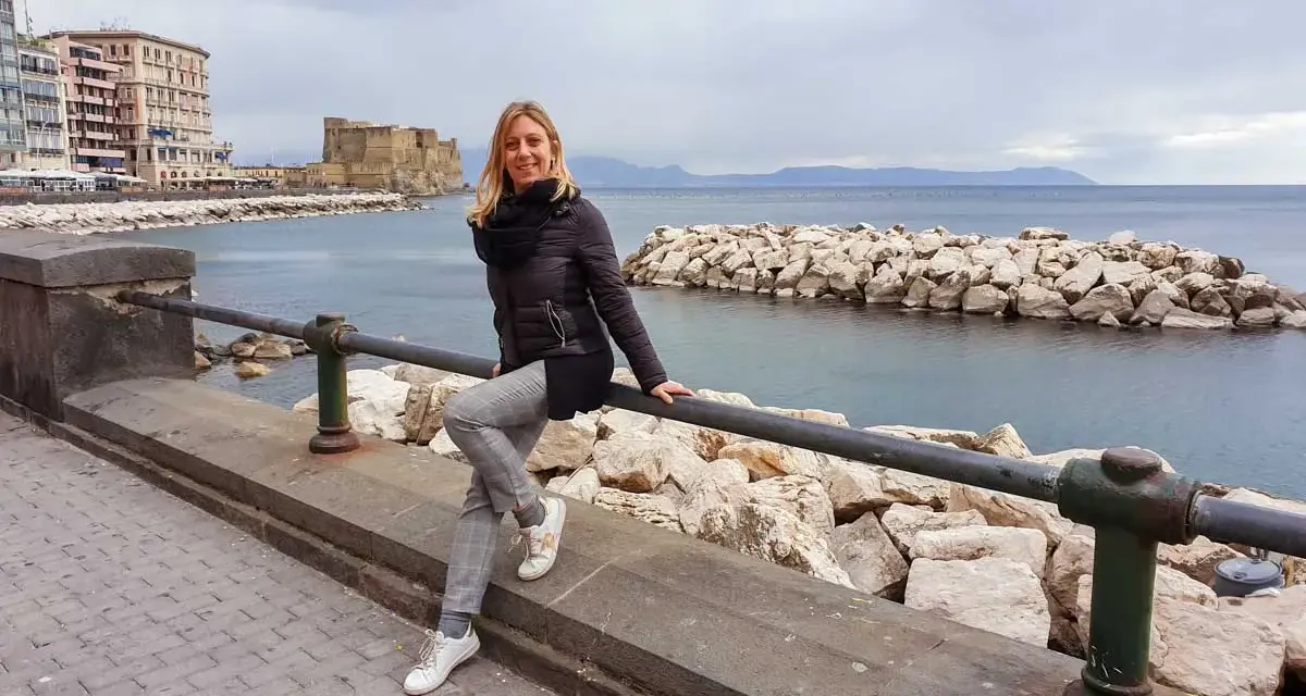 Woman sitting on a railing with Castel dell'Ovo and the sea in the background in Naples.