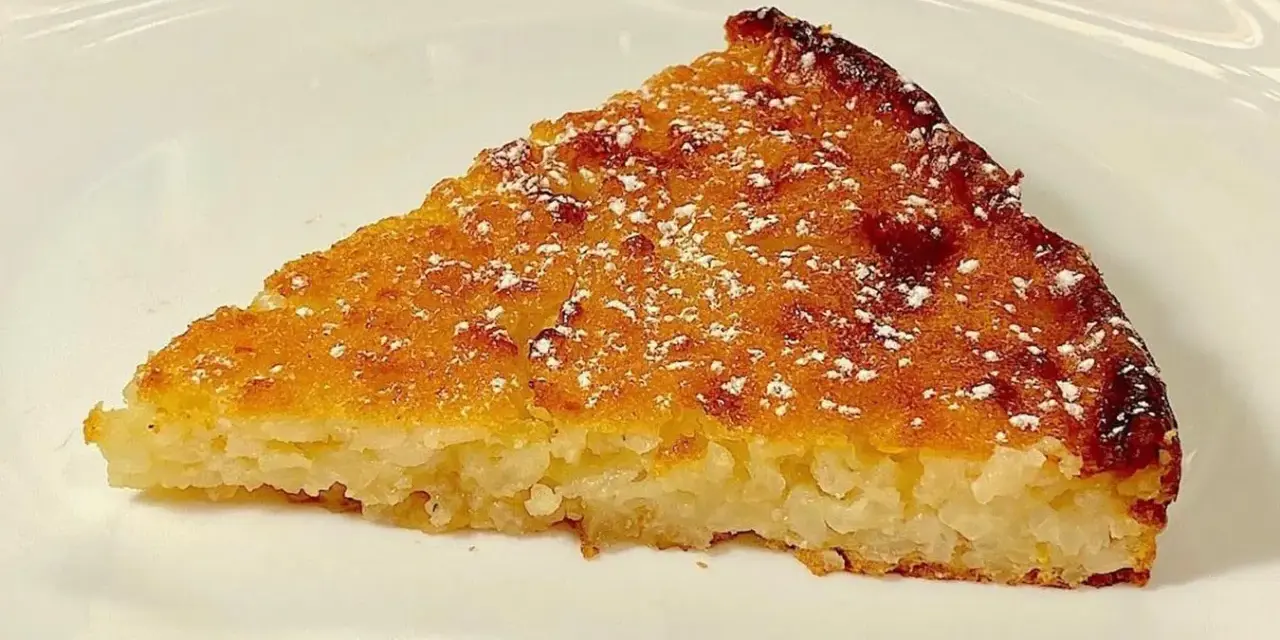 Una fetta di torta di riso, profumata e dorata, come la torta di riso ricetta della nonna, spolverata di zucchero a velo.