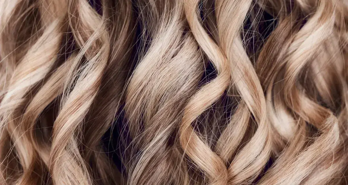 Falujące, blond włosy z subtelnymi refleksami, które mienią się w świetle, tworząc efekt głębi.
