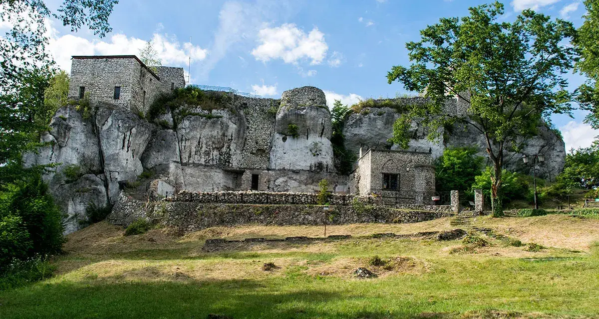 Kamienny zamek morsko wznosi się na skale, otoczony zielenią. Ruiny i mury tworzą malowniczy krajobraz.