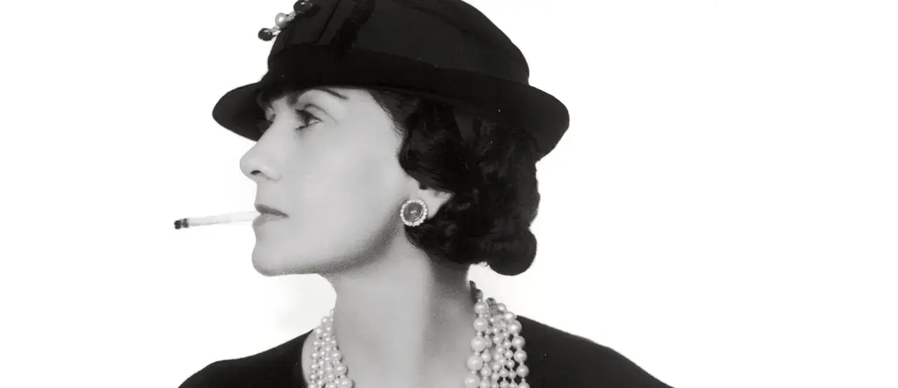 Coco Chanel, con sigaretta e perle, icona di stile, ci ricorda dove è nata Coco Chanel, un'ispirazione senza tempo.