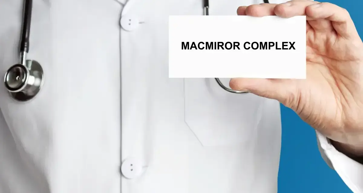 Lekarz w białym kitlu prezentuje kartkę z napisem MACMIROR COMPLEX. Stetoskop wisi na jego szyi.