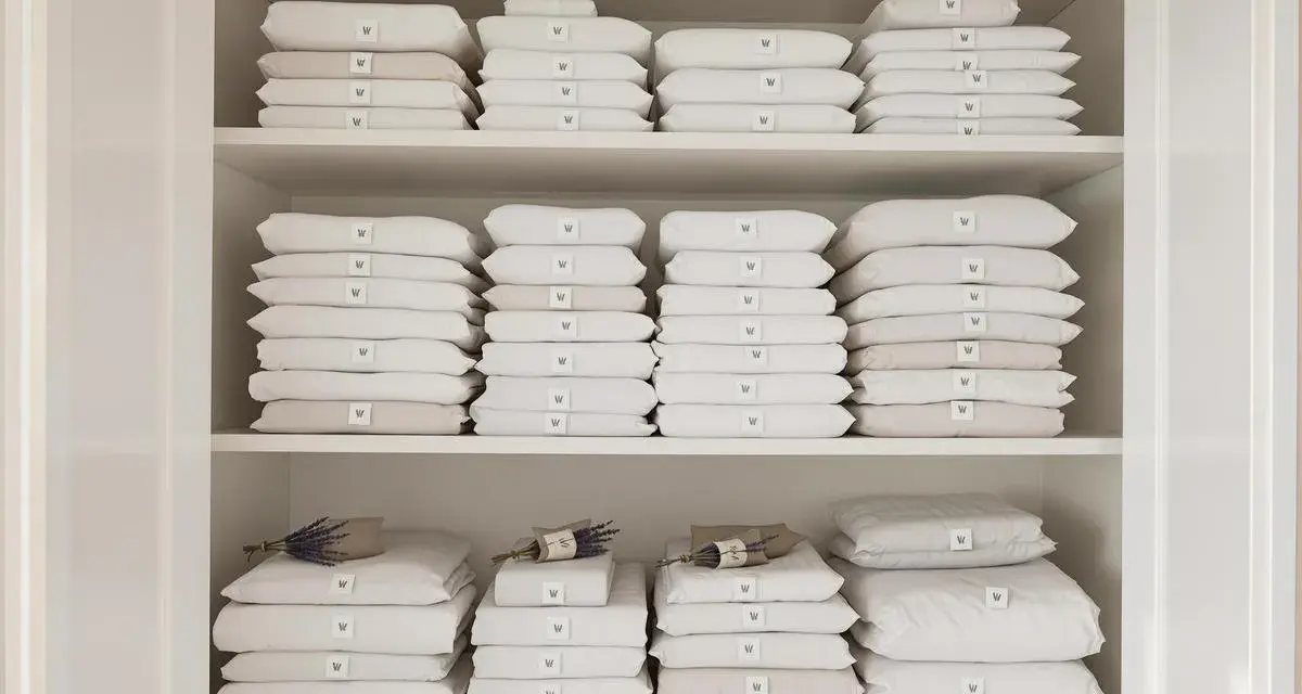 Étagères remplies de linge de lit blanc et beige plié. Une astuce rangement linge de lit pour une organisation parfaite.