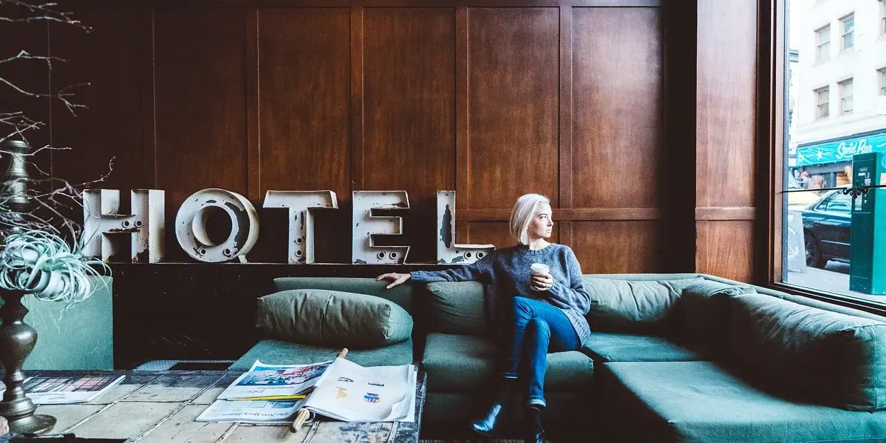 Kobieta z kawą siedzi na kanapie w hotelu. Zastanawia się, ile zarabia technik hotelarstwa.