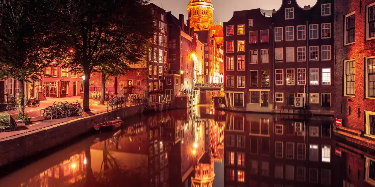 Nocny Amsterdam, kanał odbija oświetlone kamienice i kopułę kościoła. Czerwona ulica Amsterdam w blasku latarni.