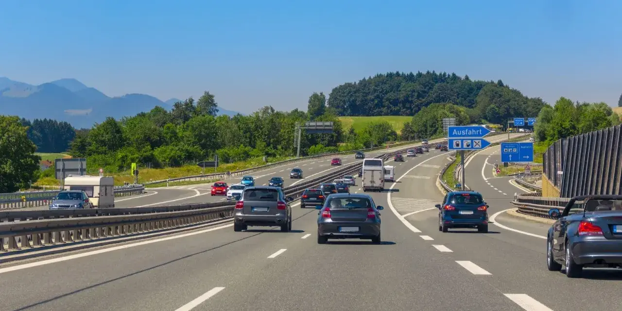 Trafik på en tysk motorväg med berg i bakgrunden. En skylt visar "Ausfahrt" (avfart), vilket indikerar en autohof i Tyskland.