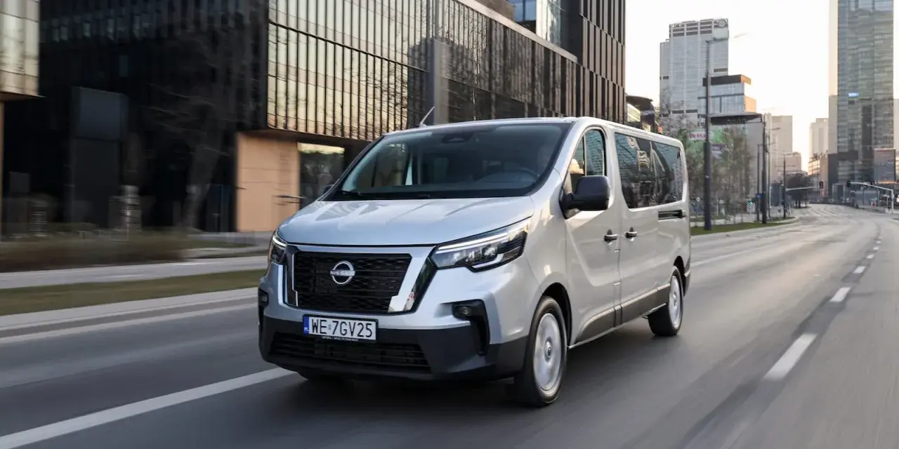 Srebrny van Nissan, jeden z najnowszych nissan modele, jedzie ulicą w nowoczesnym mieście.
