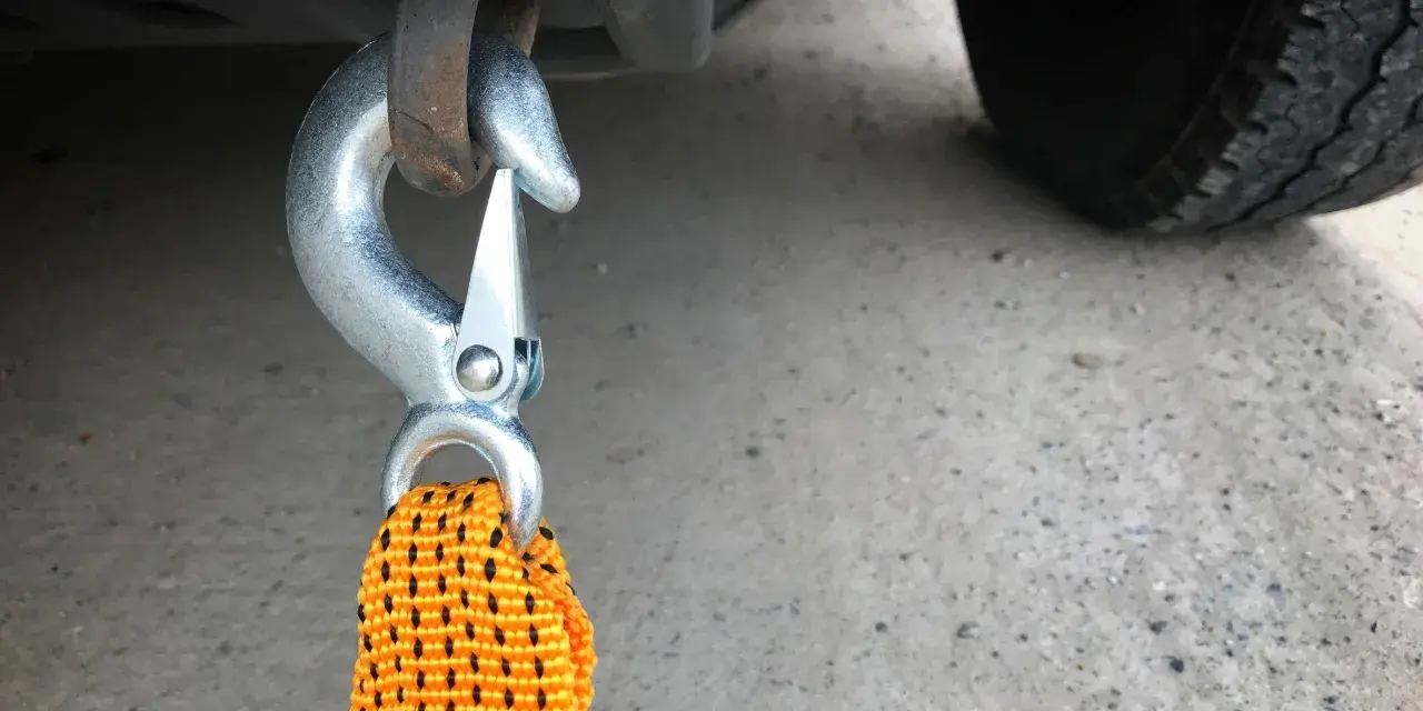 Gancio metallico agganciato al telaio di un'auto, pronto per iniziare a come trainare una macchina. La cinghia arancione è visibile.