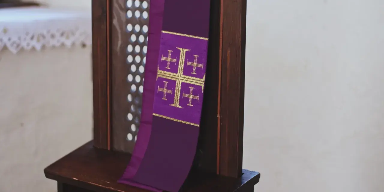Fioletowa stuła z krzyżami, symbol przygotowania do spowiedzi wielkanocnej, wisi na drewnianej kratce konfesjonału.