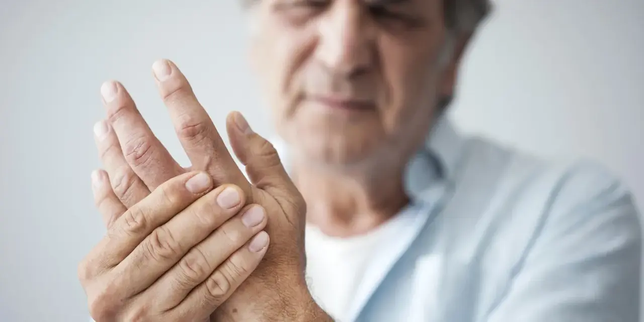 Mann hält seine Hand, da seine Finger schmerzen beim Beugen.