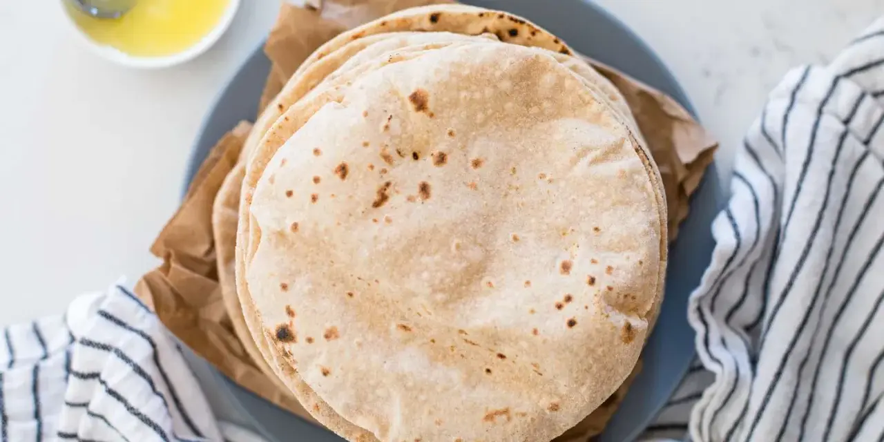 Stos świeżo upieczonych, lekko przypieczonych roti na talerzu, obok miseczki z roztopionym masłem.