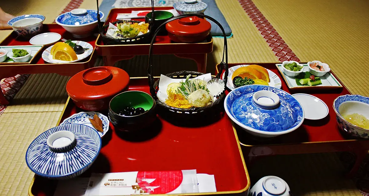 A traditional Japanese meal, perhaps a monk diet, featuring small dishes of tempura, fruit, pickles, and black beans on red lacquer trays.