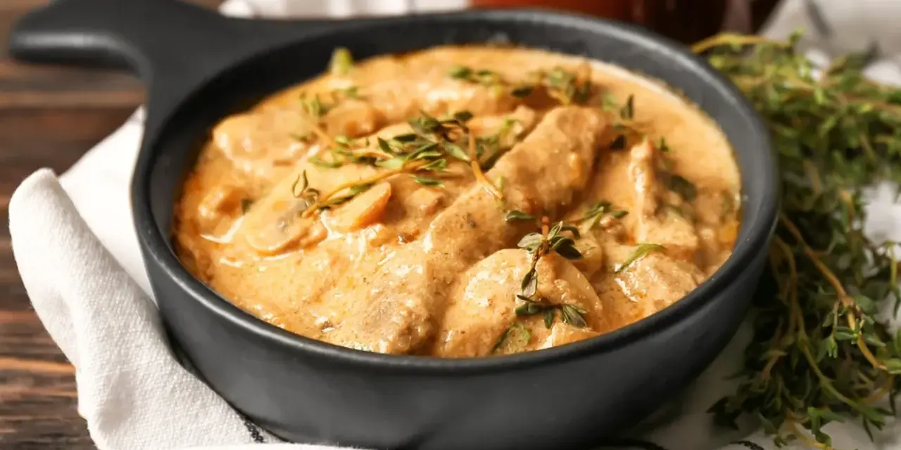 Cremiges Rindfleisch mit Pilzen, garniert mit frischem Thymian. Ein köstliches stroganoff rezept original, serviert in einer schwarzen Schüssel.