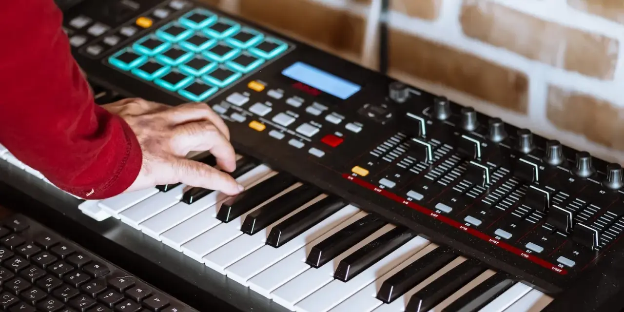 Hand spielt auf einem Keyboard, das für die Erzeugung von Synth-Musik verwendet wird. Viele Knöpfe und Pads sind sichtbar.