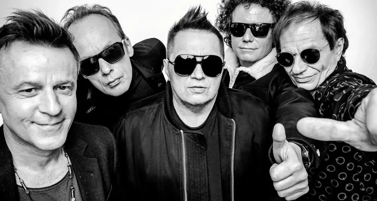 Pięciu mężczyzn w okularach przeciwsłonecznych, gotowych na koncert. Jeden z nich pokazuje kciuk w górę, jakby mówił "t.love hau! hau!".