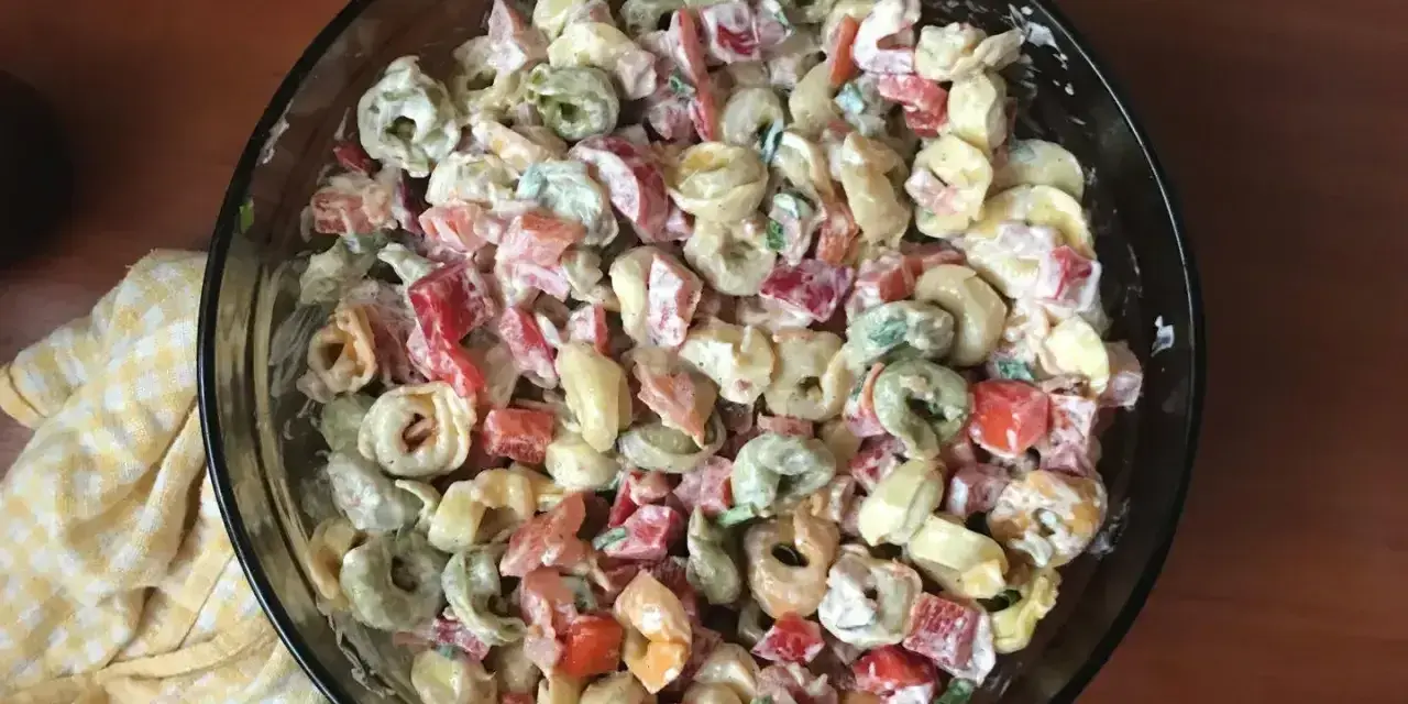 Kolorowa sałatka z tortellini, papryką i majonezem w szklanej misce.