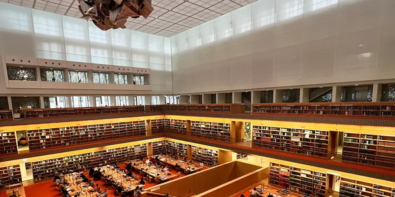 Große Bibliothek mit vielen Regalen voller Bücher. Menschen sitzen an Tischen und lesen. Ein Ort für Lesungen in Berlin.