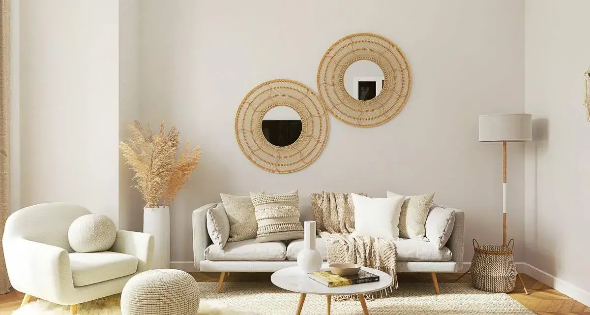 Salón acogedor con butaca blanca y sofá gris, decorado con espejos de mimbre y plantas secas. La combinación de sofá y butaca crea un espacio perfecto para relajarse.
