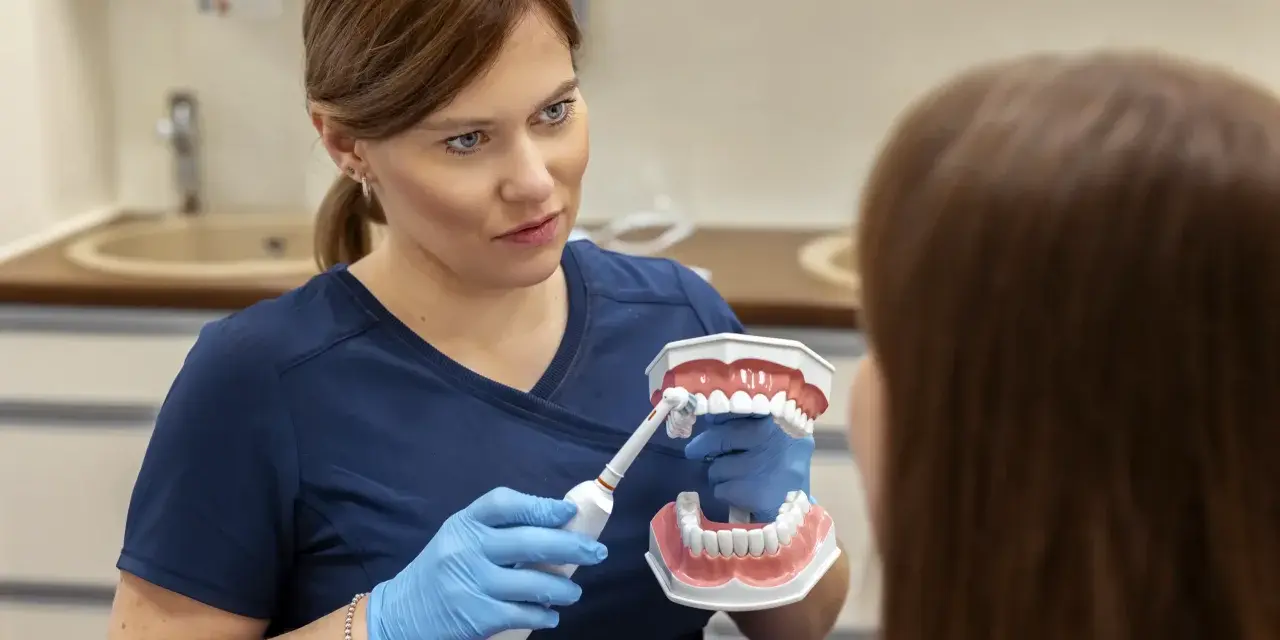 Dentystka pokazuje na modelu, dlaczego myjemy zęby, używając szczoteczki elektrycznej.