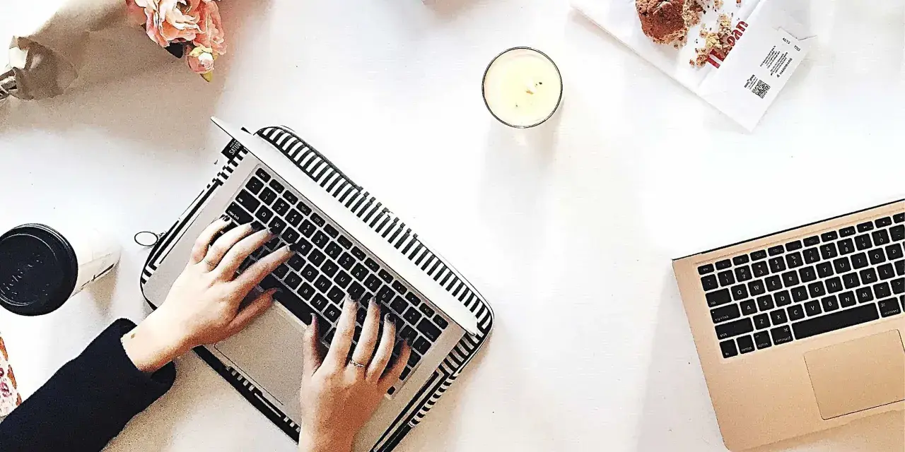 Kobieta pisze na laptopie, przygotowując wypowiedzenie umowy o dzieło. Obok świeca, muffinka i bukiet kwiatów.