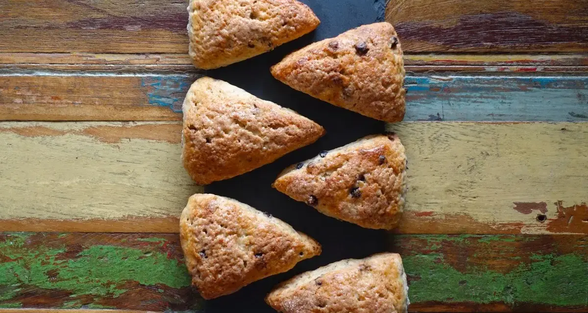 Sechs dreieckige Schokoladen-Scones liegen auf einem rustikalen Holztisch. Perfekt für alle, die keine komplizierten discard rezepte mögen.