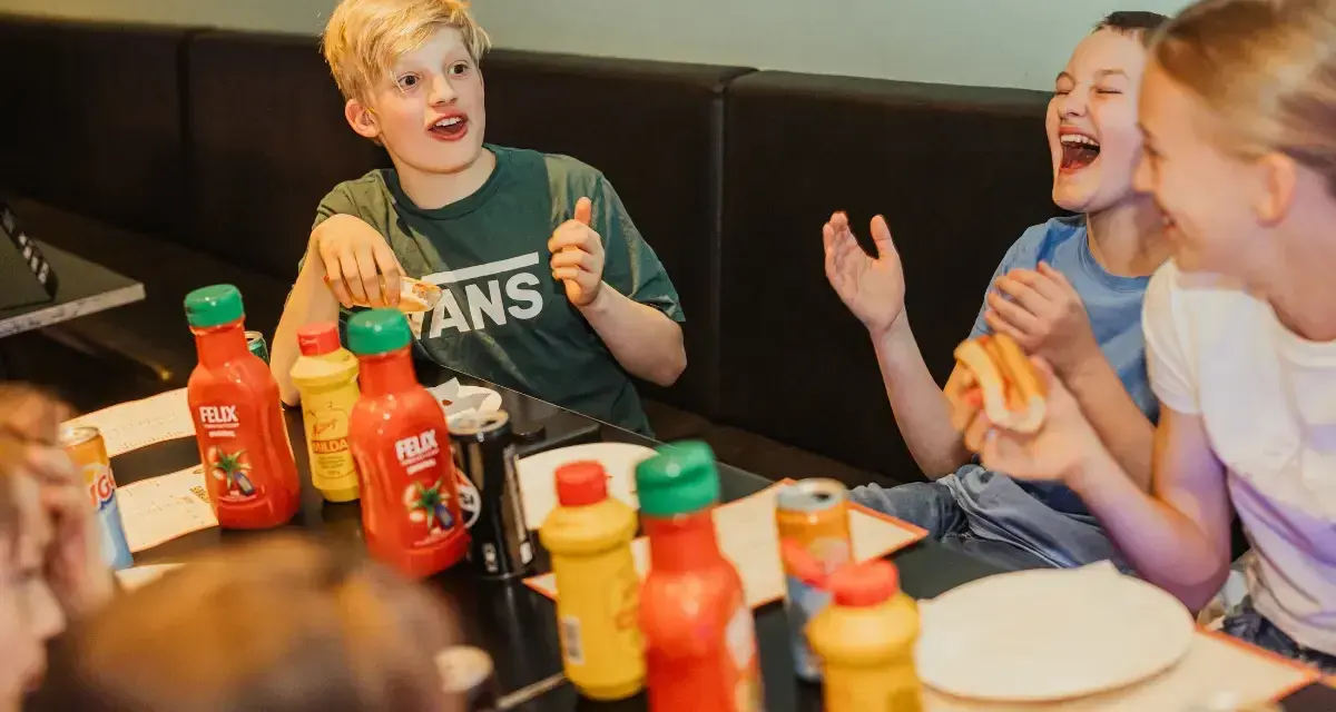 Barn skrattar och äter korv med bröd vid ett bord med Felix ketchup och senap. Perfekt för tips på femkamp!