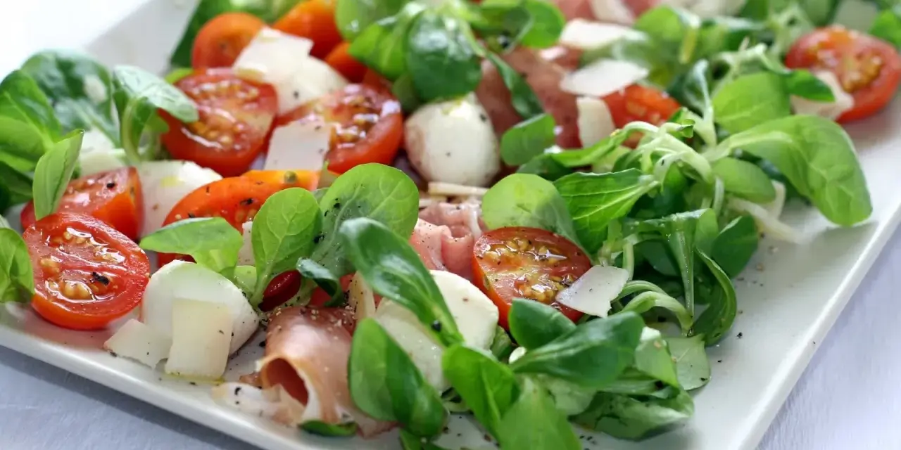Pyszna sałatka z szynką parmeńską, pomidorkami koktajlowymi, mozzarellą i świeżą rukolą. Idealna na lekki posiłek.