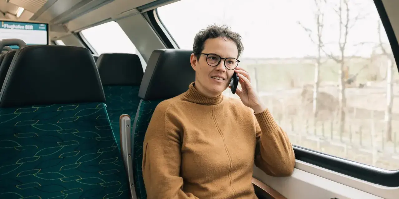 Kobieta w brązowym swetrze rozmawia przez telefon w pociągu. Czas na moją kolej, by usiąść przy oknie i podziwiać widoki.