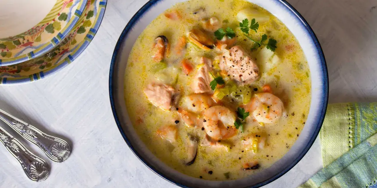 Sopa cremosa de pescado con salmón, gambas y mejillones, decorada con perejil.