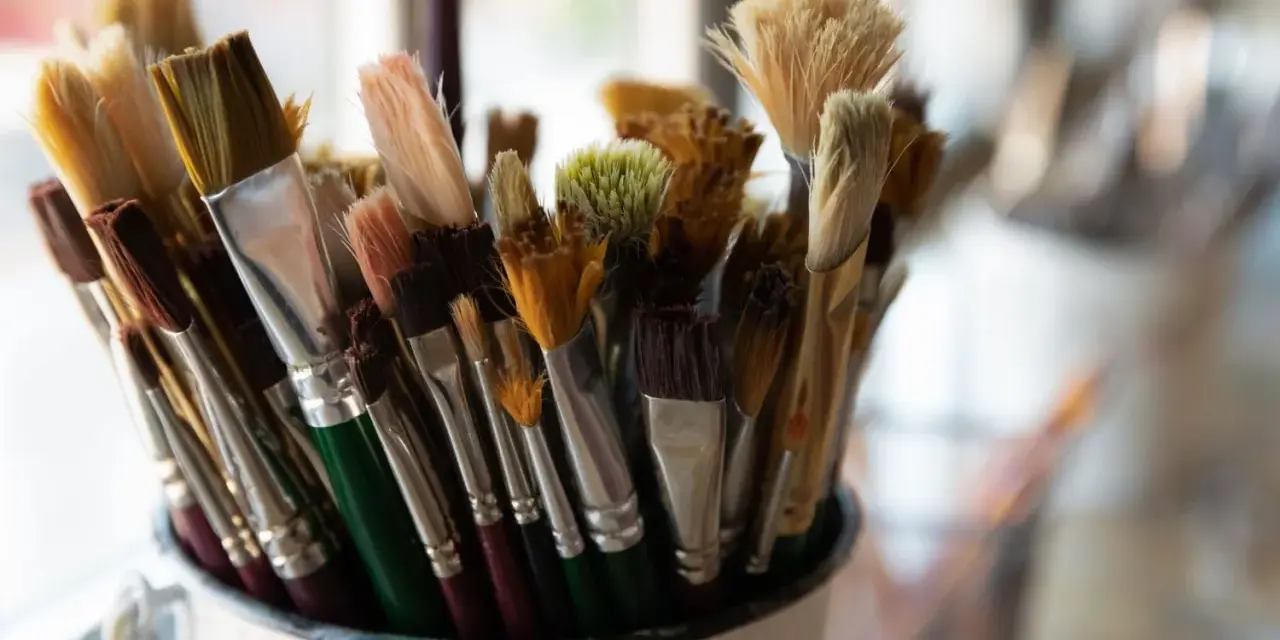 Gros plan sur un pot rempli de pinceaux de peinture aux poils variés, certains neufs, d'autres usagés.
