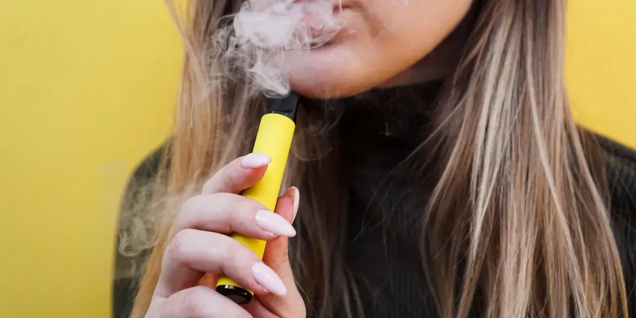 Mujer exhala vapor de un vaper sin nicotina, pero ¿sabías que el vaper sin nicotina mancha los dientes?