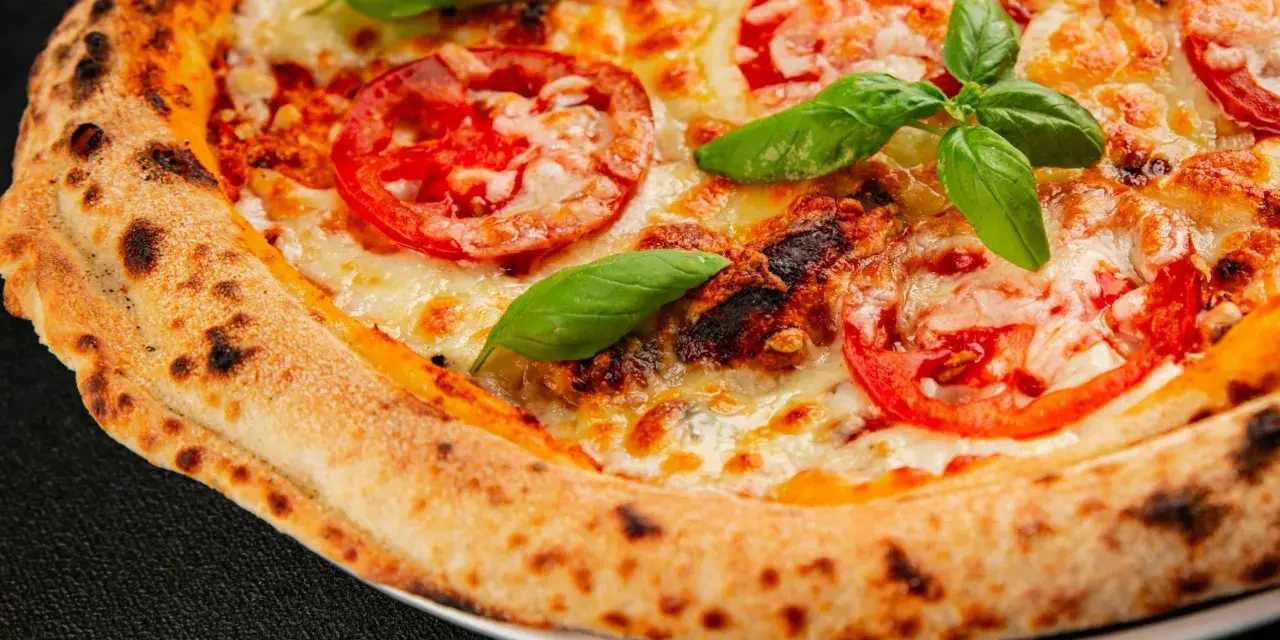 Pyszna pizza Margherita z pomidorami i bazylią, idealnie wypieczona w wysokiej temperaturze przez kilka minut.