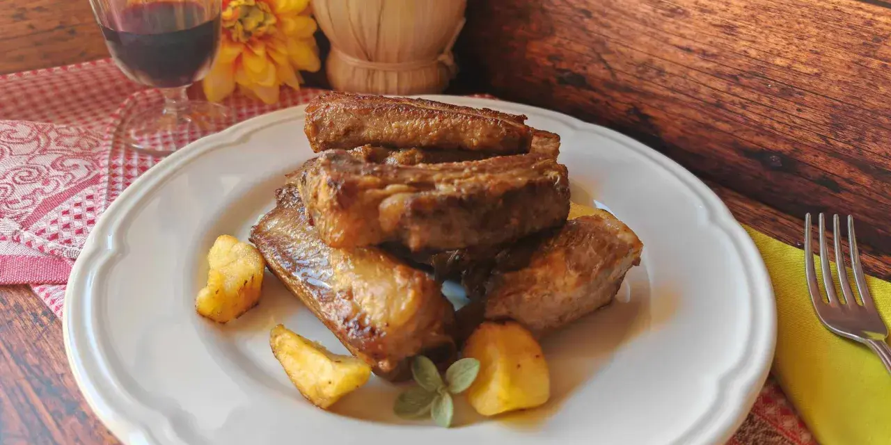 Succulente costine di maiale in padella, dorate e saporite, servite con patate arrosto e un rametto di salvia.
