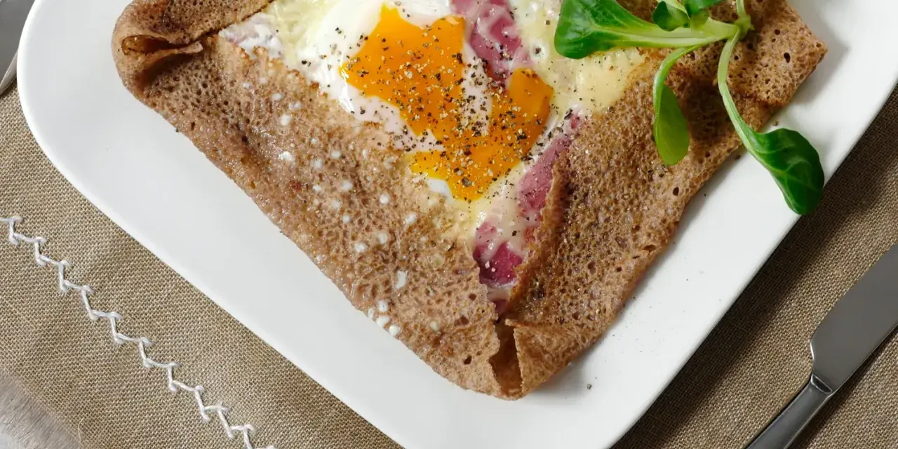 Une galette bretonne garnie d'un œuf, de jambon et de fromage, poivrée et décorée d'une feuille verte. Un délice de french crepes !