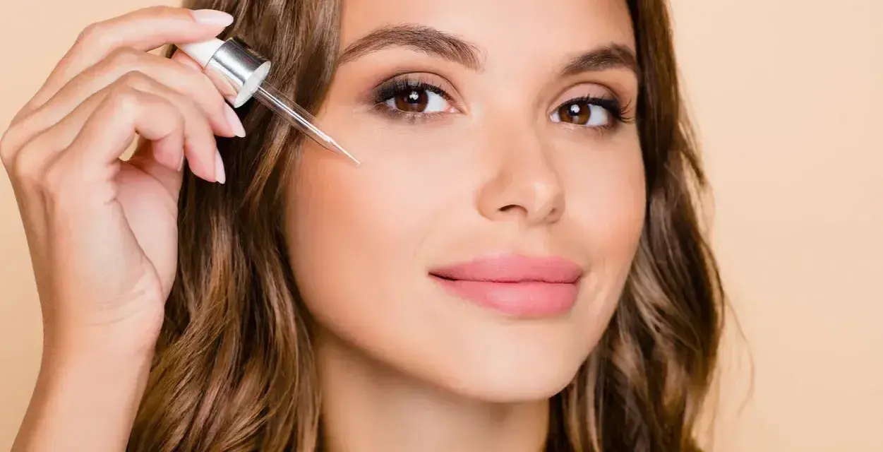 Kobieta aplikuje serum z pipetką na policzek. Dowiedz się, jak stosować retinol dla pięknej cery.