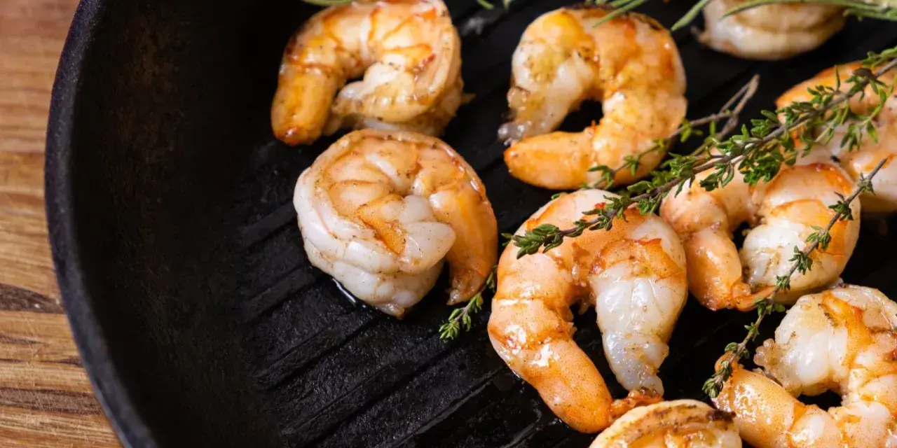 Gambas a la plancha jugosas y doradas, con ramitas de tomillo fresco sobre una sartén de hierro fundido.