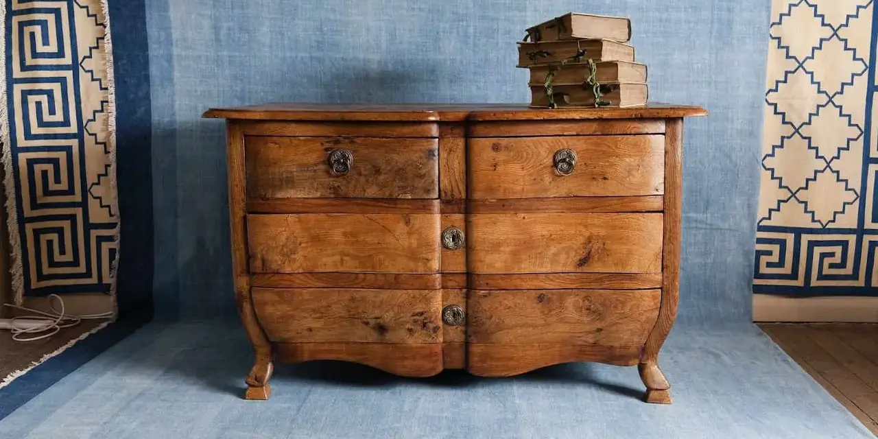 Cómoda de madera antigua, lista para pintar. Unos libros viejos descansan sobre ella.