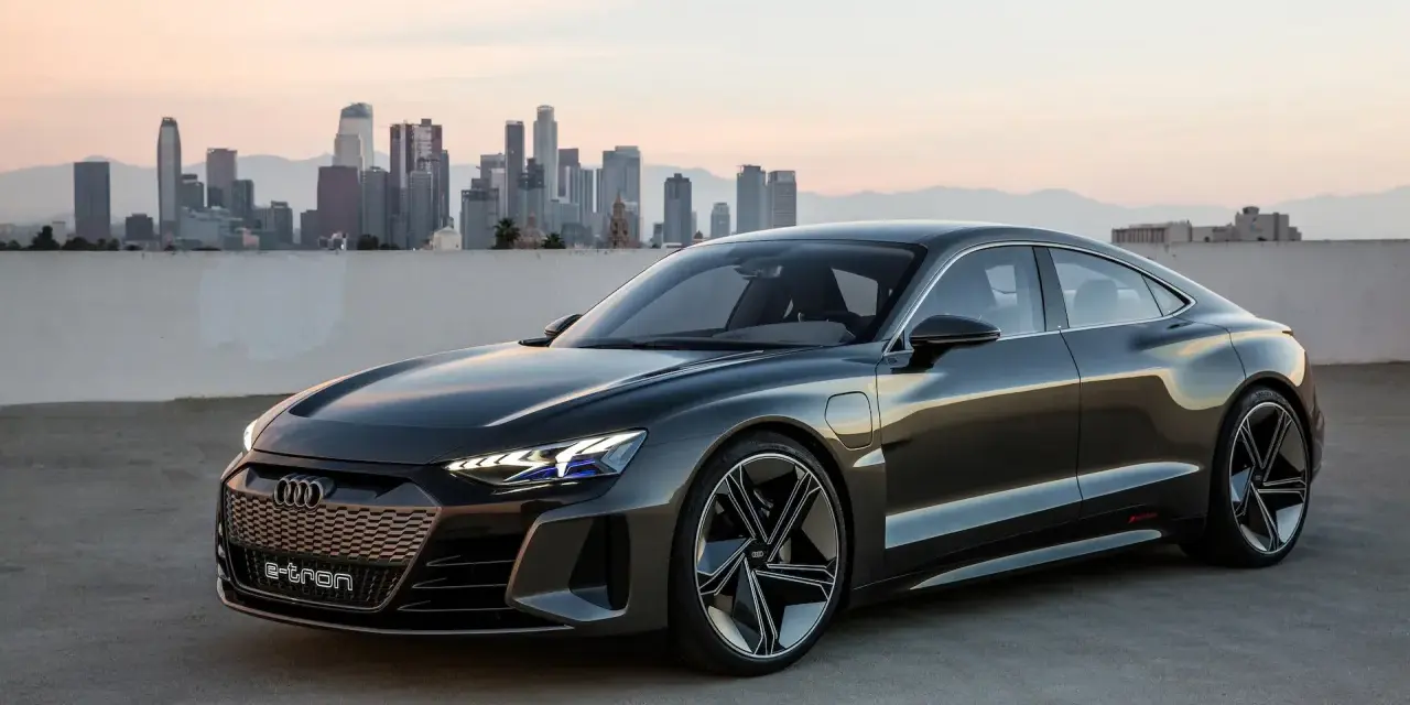 Ciemnoszary Audi e-tron GT stoi na tle panoramy miasta o zachodzie słońca.