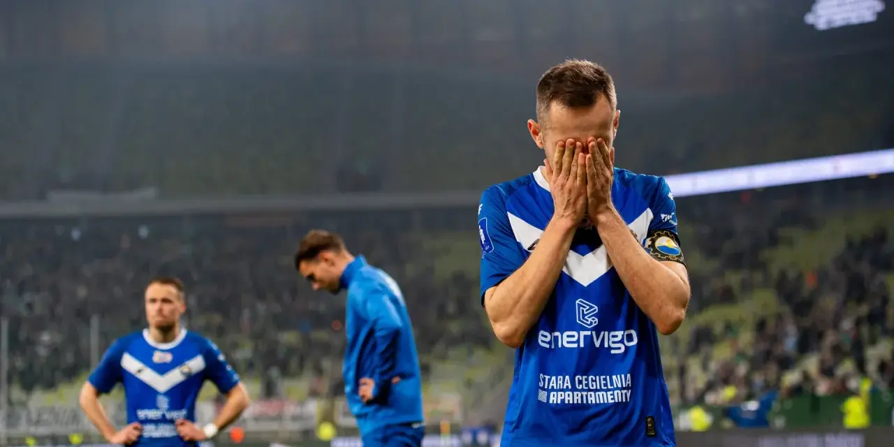 Piłkarz w niebieskiej koszulce z napisem "enerVigo" zakrywa twarz dłońmi. W tle inni zawodnicy i trybuny. Emocje po przegranym meczu w I lidze piłki ręcznej.