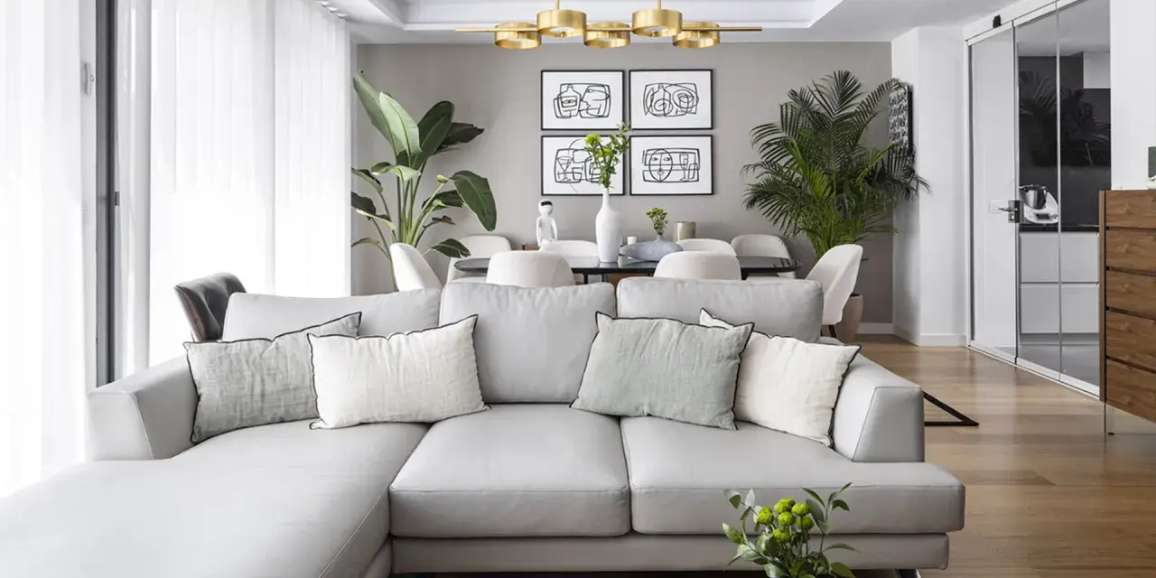Sofá gris y plantas verdes, ideas de colores para pintar salones pequeños. Paredes neutras y suelo de madera.
