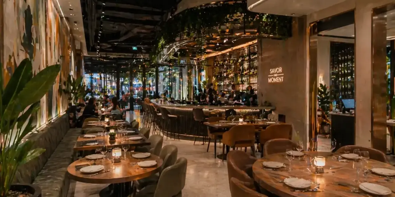Elegantes mesas y un bar iluminado, con arte mural y plantas, ofrecen **ideas decoración restaurante** acogedoras.