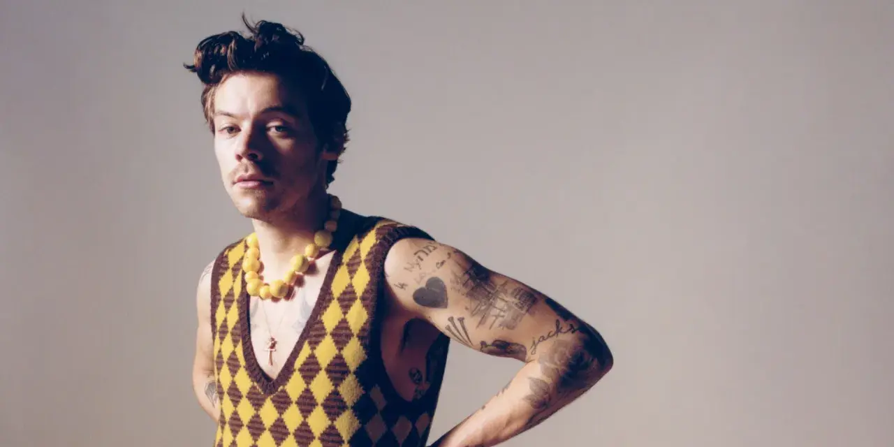 Harry Styles w kamizelce w romby i żółtym naszyjniku, jakby inspirował nowe harry styles utwory.